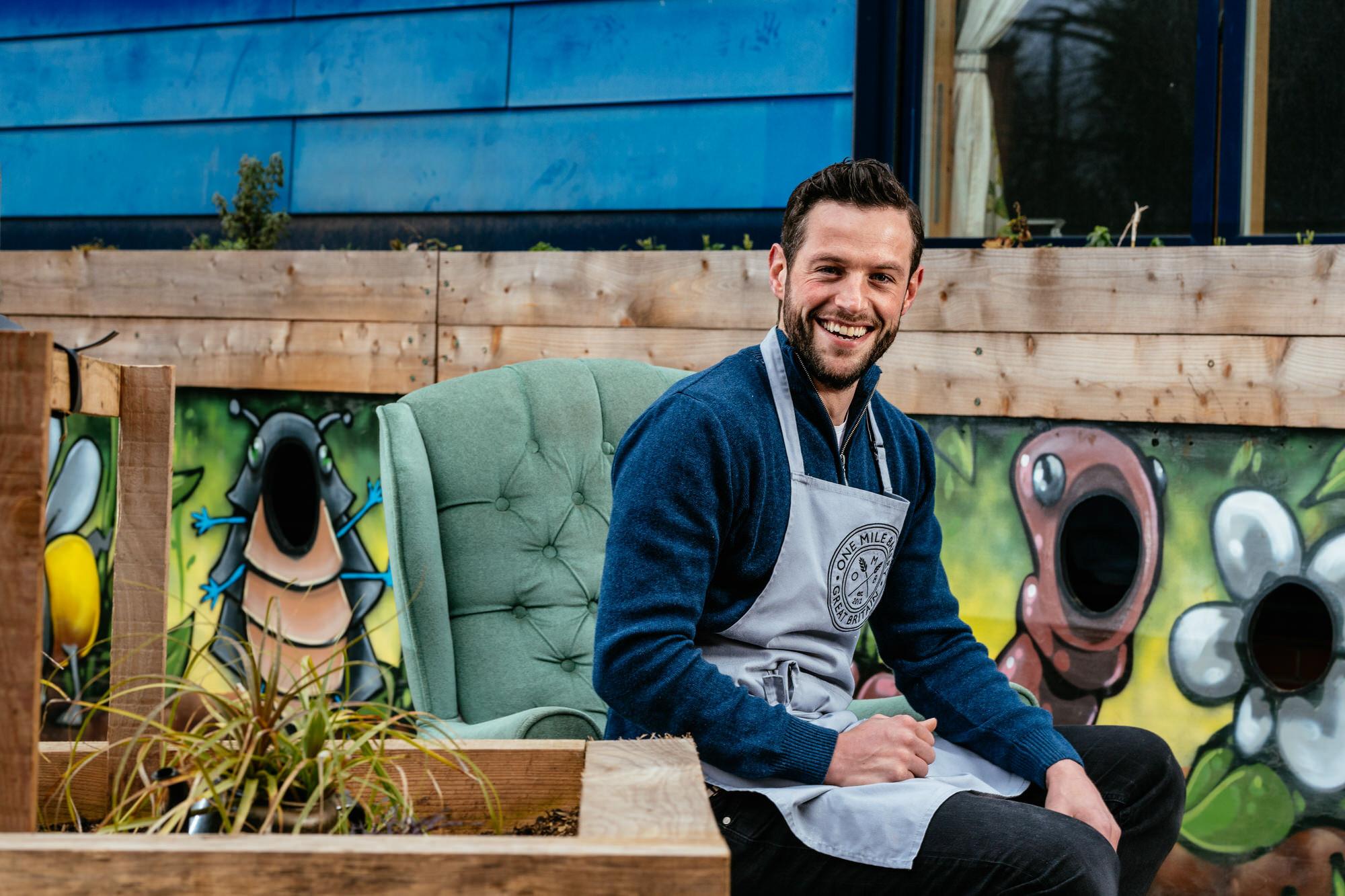 portrait of a man sat in a chair wearing an apron
