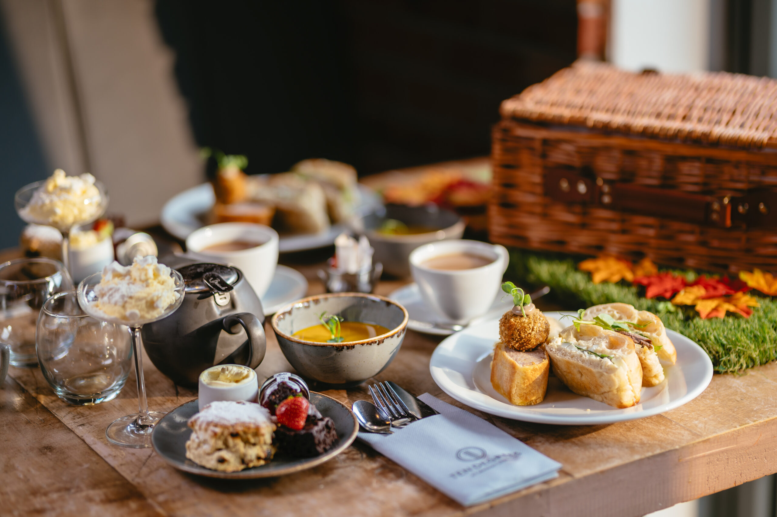A table with several drinks and dishes of food with a hamper
