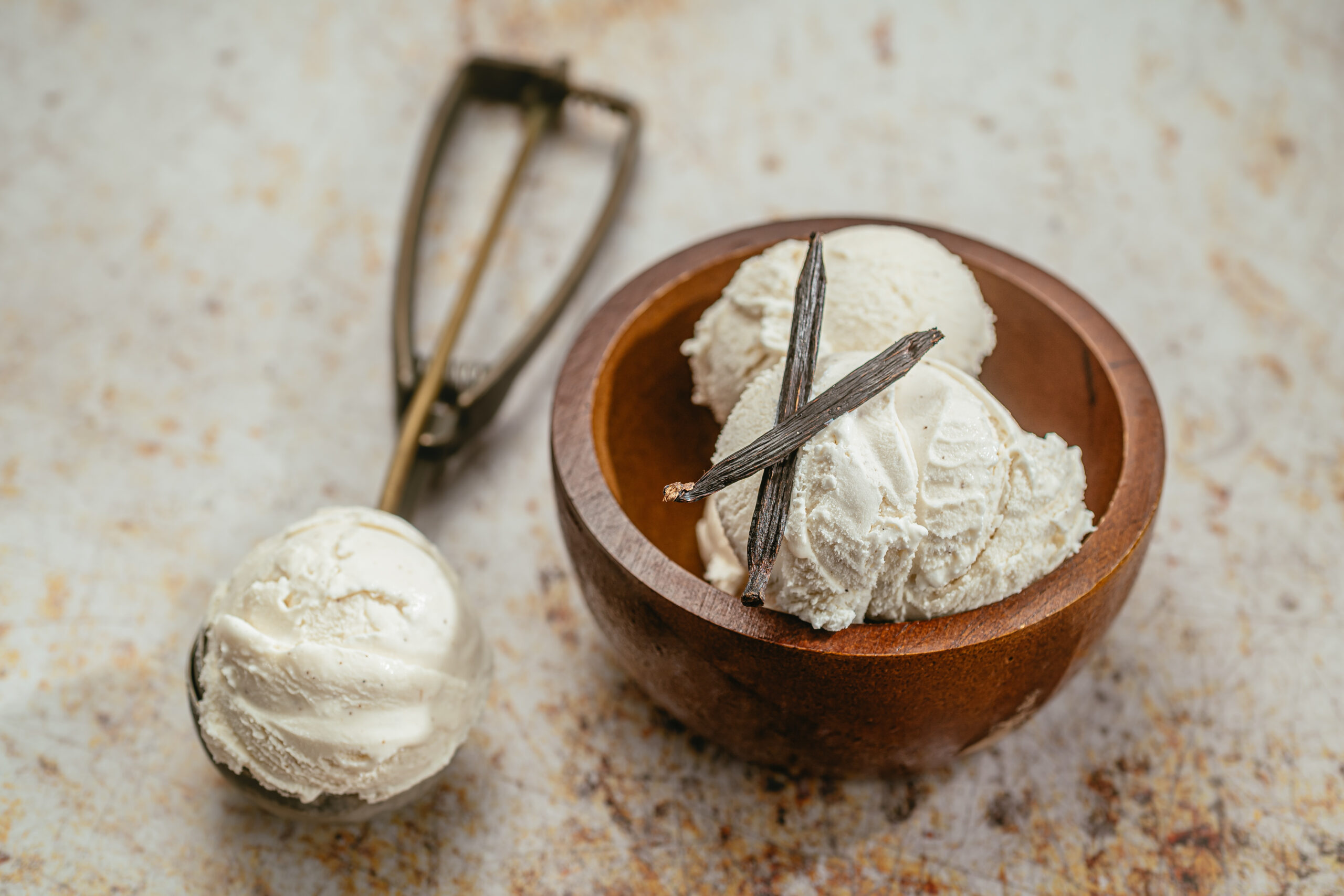 Food photograph of ice cream in wooden bowl and an ice cream scoop